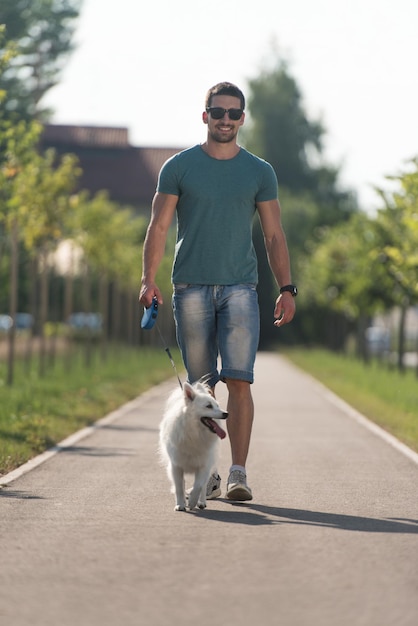 Junger Mann und deutscher Spitz gehen im Park spazieren, er hält den Hund an der Leine