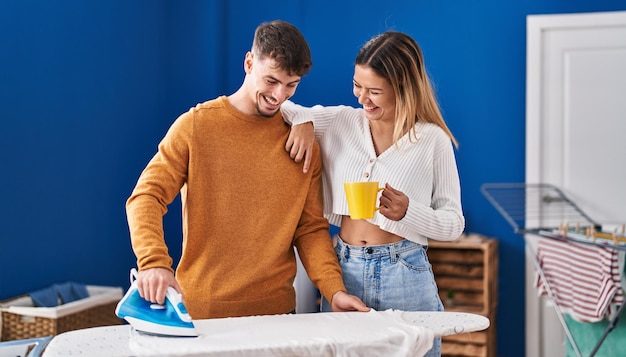 Junger Mann und Frau bügeln Kleidung und trinken Kaffee in der Waschküche