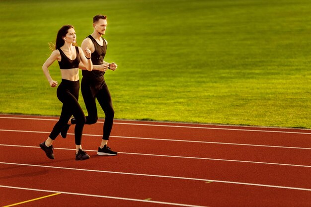 Junger Mann und Frau, die auf der Rennstrecke im Stadion laufen Junge männliche und weibliche Athleten, die zusammen üben