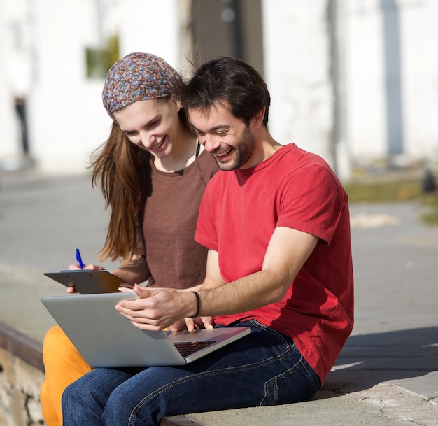 Junger Mann und Frau, die draußen am Laptop lächelt