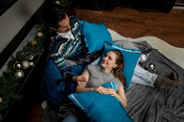 Junger Mann und Frau in der Liebe sitzen auf dem Boden in ihrem Wohnzimmer mit Kissen und Weihnachtsschmuck.