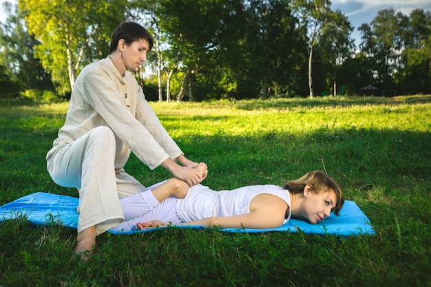 Junger Mann und Frau in einem weißen Gewand, die Thai-Massage mit Yoga-Übungen auf der Matte machen