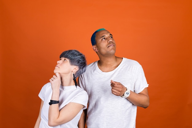 Junger Mann und Frau in lässigem Weiß auf orangefarbener Wand nachdenklicher Blick beiseite mit Kinn