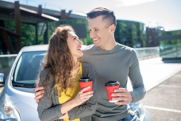 Junger Mann und Frau mit Kaffee nahe einem Auto