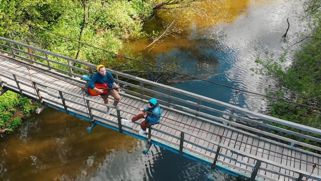 Junger Mann und Frau Reisende auf der Brücke Mann spielt Gitarre und Frau sitzt auf der Brücke