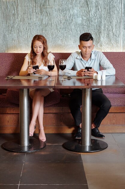 Junger Mann und Frau sitzen am Tisch im Restaurant und checken Social Media, anstatt zu reden