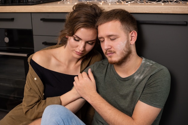 Junger Mann und Frau sitzen auf Boden in der Küche. Liebevolles junges Paar, das Zeit zusammen zu Hause verbringt.