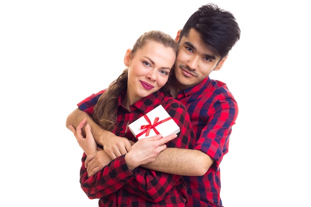 Junger mann und junge glückliche frau mit weißem kleinen geschenk in roten karierten hemden, die sich umarmen