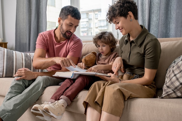 Junger Mann und sein kleiner Sohn zeigen auf Seite der offenen Enzyklopädie, während Vater das Thema des Artikels oder der merkwürdigen Tatsachen erklärt