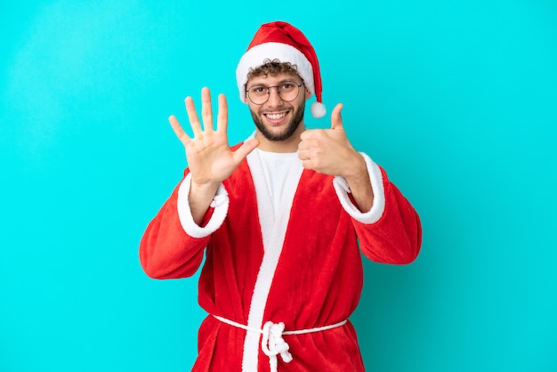 Junger Mann verkleidet als Weihnachtsmann auf blauem Hintergrund isoliert und zählt sechs mit den Fingern