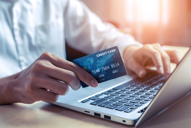 Junger Mann verwendet Kreditkarte für Online-Shopping-Zahlungen auf Laptop-Computer-Anwendung oder Website. E-Commerce- und Online-Shopping-Konzept.