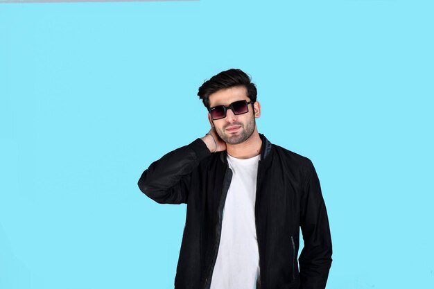 junger Mann vorne Pose mit Winterkleidung und Brille auf blauem Hintergrund indisches pakistanisches Modell