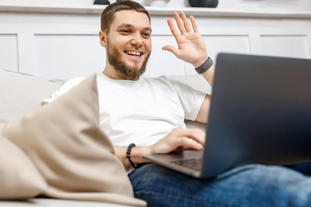 Junger Mann zu Hause auf der Couch, der per Video mit einem Laptop spricht