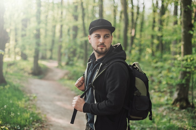 Junger Mannreisender, der im Wald mit Bagpack geht