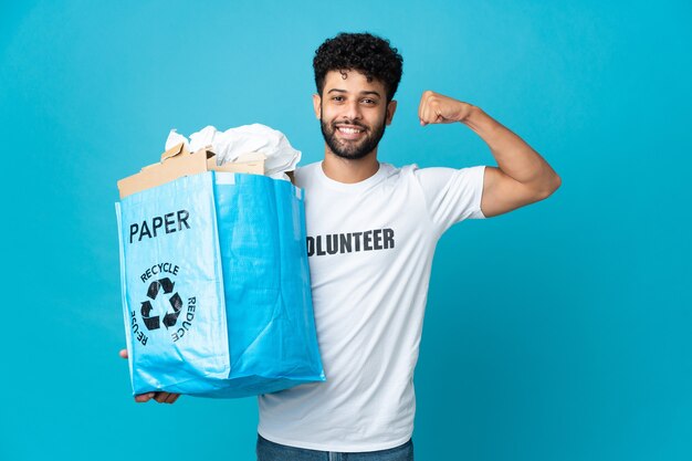 Junger marokkanischer Mann, der einen Recyclingbeutel voll Papier hält, um isoliert zu recyceln