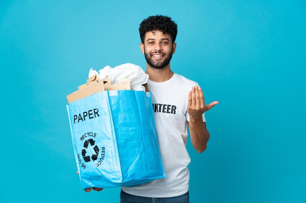 Junger marokkanischer Mann, der einen Recyclingbeutel voll Papier hält, um isoliert zu recyceln