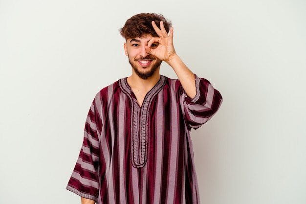 Junger marokkanischer Mann isoliert auf weiß aufgeregt, ok Geste auf Auge haltend.