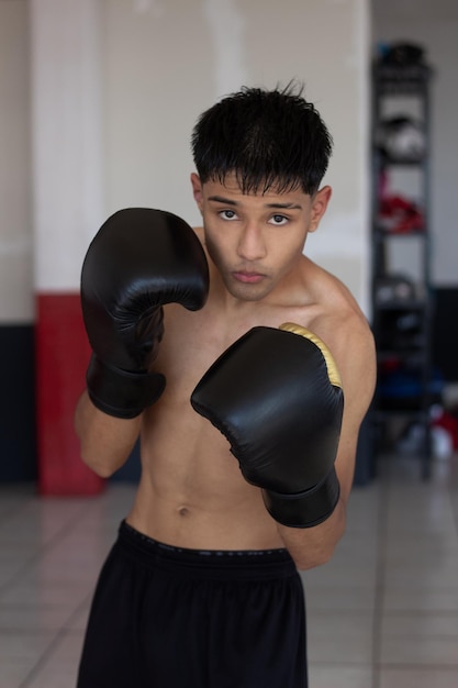 Junger mexikanischer Boxer posiert in Wachposition und schaut in Kampfposition in die Kamera