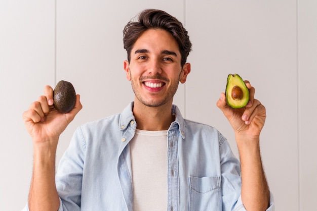 Junger Mischlingsmann, der Avocados in seiner Küche hält