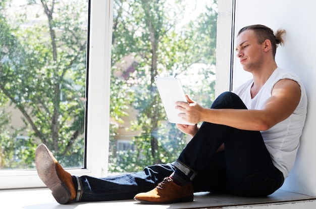 Junger Modemann, der nahe Fenster mit Tablette sitzt. Lifestyle-Konzept.