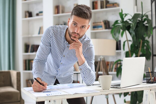 Junger moderner Geschäftsmann, der Daten mit Laptop analysiert, während er im Büro arbeitet.