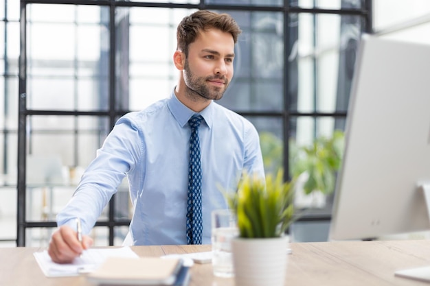 Junger moderner Geschäftsmann, der mit dem Computer arbeitet, während er im Büro sitzt