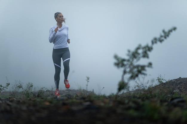 Junger motivierter Läufer, der während des kalten, nebligen Morgens in der Natur joggt Platz kopieren