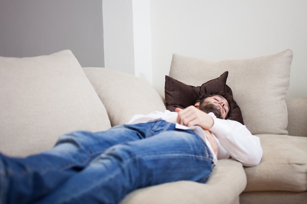 Junger müder Mann, der zu Hause auf seiner Couch schläft