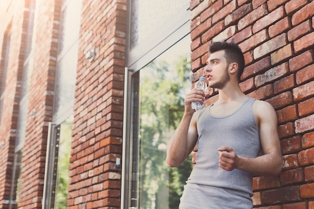 Junger müder Mannläufer macht Pause, trinkt Wasser nach dem Joggen im Stadtzentrum, Kopierraum