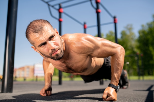 Junger muskulöser Bodybuilder, der auf Fäusten über Boden steht, während Liegestütze während des Trainings im Freien machen