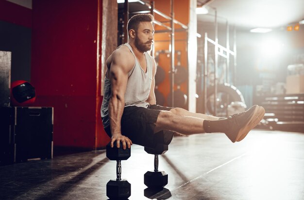 Junger muskulöser Mann, der im Fitnessstudio hart trainiert. Sein ganzes Gewicht liegt auf Hanteln.