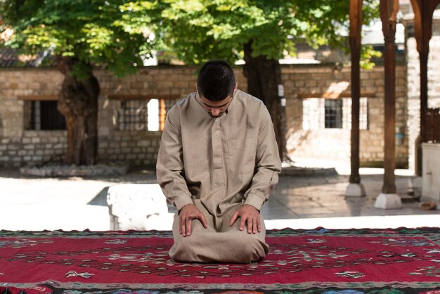 Junger muslimischer Mann, der traditionelles Gebet zu Gott macht, während er eine traditionelle Kappe Dishdasha trägt