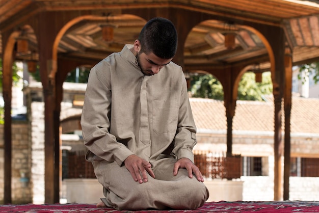 Junger muslimischer Mann, der traditionelles Gebet zu Gott macht, während er eine traditionelle Kappe Dishdasha trägt