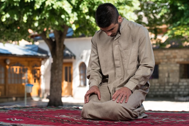 Junger muslimischer Mann, der traditionelles Gebet zu Gott macht, während er eine traditionelle Kappe Dishdasha trägt