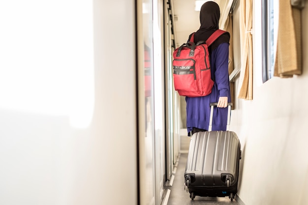 Junger muslimischer Reisender mit rotem Rucksack und Koffer im Zug.