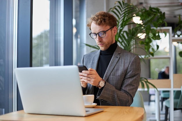 Junger nachdenklicher Geschäftsmann, der SMS mit dem Handy liest, Kommunikation im Büro arbeitet