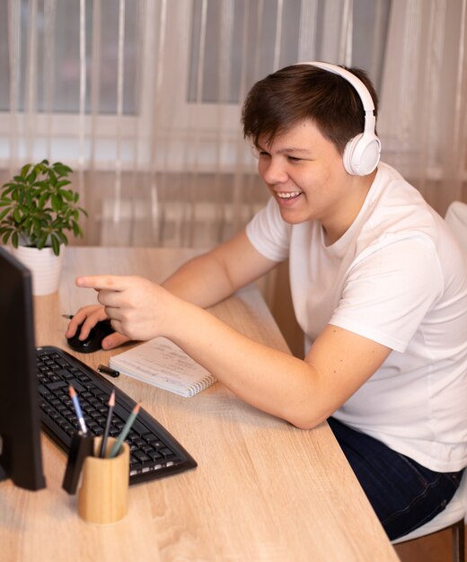 Junger niedlicher glücklicher Mann in Jeans, weißem T-Shirt und Kopfhörern, die am Tisch lächelnd sitzen