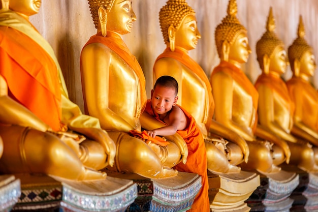 Junger Novizenmönch, der Buddha-Statue am alten Tempel in Thailand scheuert