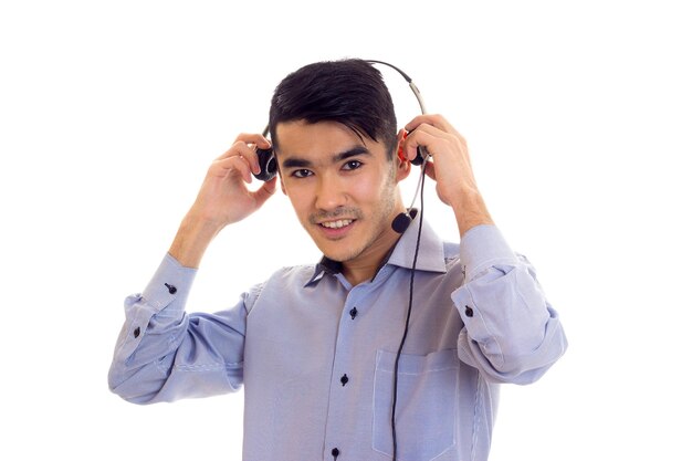 Junger optischer Timman mit dunklem Haar im blauen Hemd mit schwarzen Kopfhörern auf weißem Hintergrund im Studio