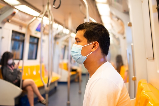 Junger Passagier mit medizinischer Gesichtsschutzmaske, der in der U-Bahn oder im Skytrain sitzt