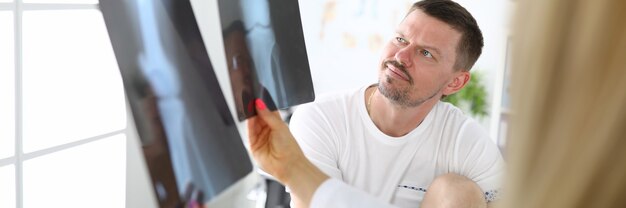 Foto junger patient mit wundem bein betrachtet röntgenaufnahme des kniegelenks mit arzt in der klinik