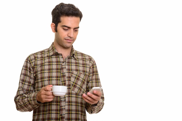 Junger persischer Mann, der Handy verwendet, während Kaffeetasse lokalisiert hält