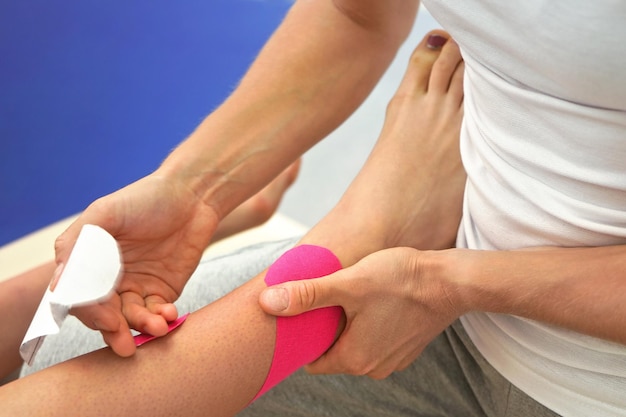 Junger Physiotherapeut, der rosafarbenes Kinesiologie-Klebeband auf die Füße oder das Knie der Patientin aufträgt, Nahaufnahmedetail