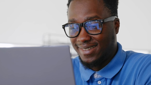 Junger positiver Afro-Geschäftsmann arbeitet am Schreibtisch im Büro mit Laptop