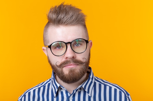 Junger positiver trendiger Mann-Hipster mit einem Schnurrbartbart und einer Fetisch-Halskette im Hemd, das auf a aufwirft