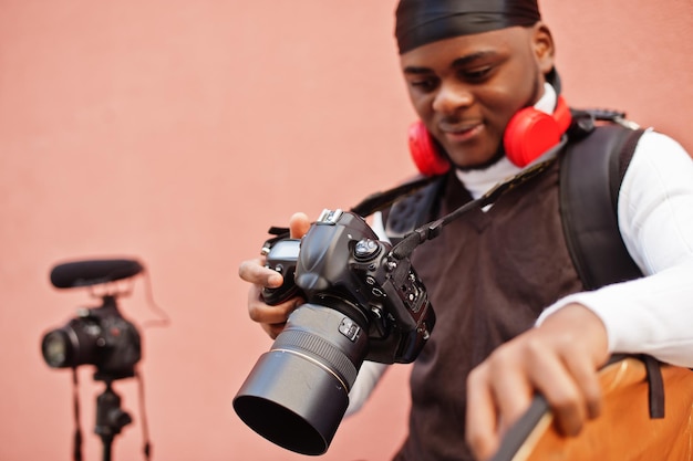 Junger professioneller afroamerikanischer Videofilmer, der eine professionelle Kamera mit professioneller Ausrüstung hält Afro-Kameramann mit schwarzem Duraq, der Videos macht