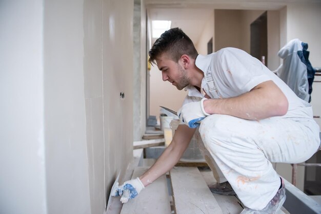 Foto junger professioneller bauarbeiter verputzt gipswände in der neuen großen, modernen wohnung auf zwei ebenen