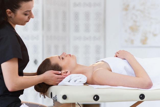 Junger professioneller Masseur, der Massage für verschlafene kaukasische Frau auf dem weißen Raumhintergrund macht.