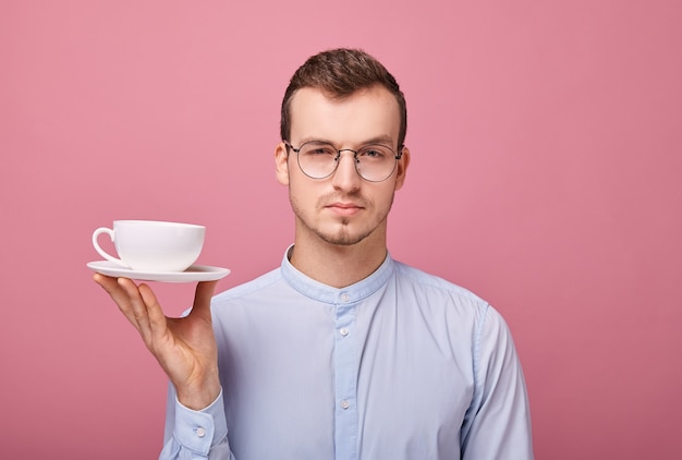 Junger Professor in den Gläsern, die nach der Arbeit bei einem weißen Becher Kaffee in seiner Hand liegen