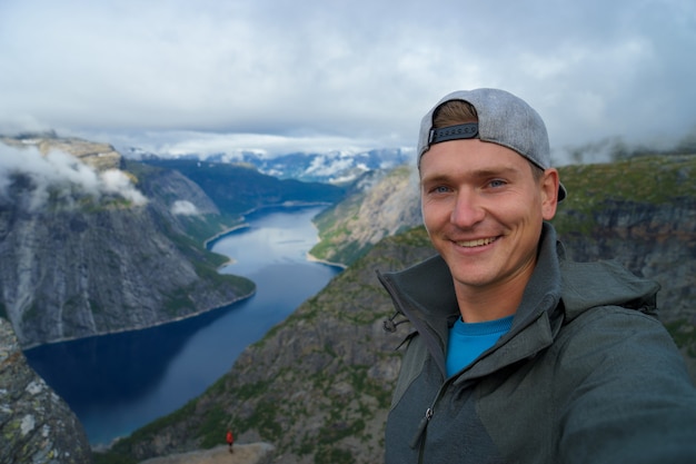 Junger Reisender, der Mütze und warmen Mantel trägt und Selfie auf der Oberseite mit schönem Fjord auf Oberfläche in Norwegen nimmt